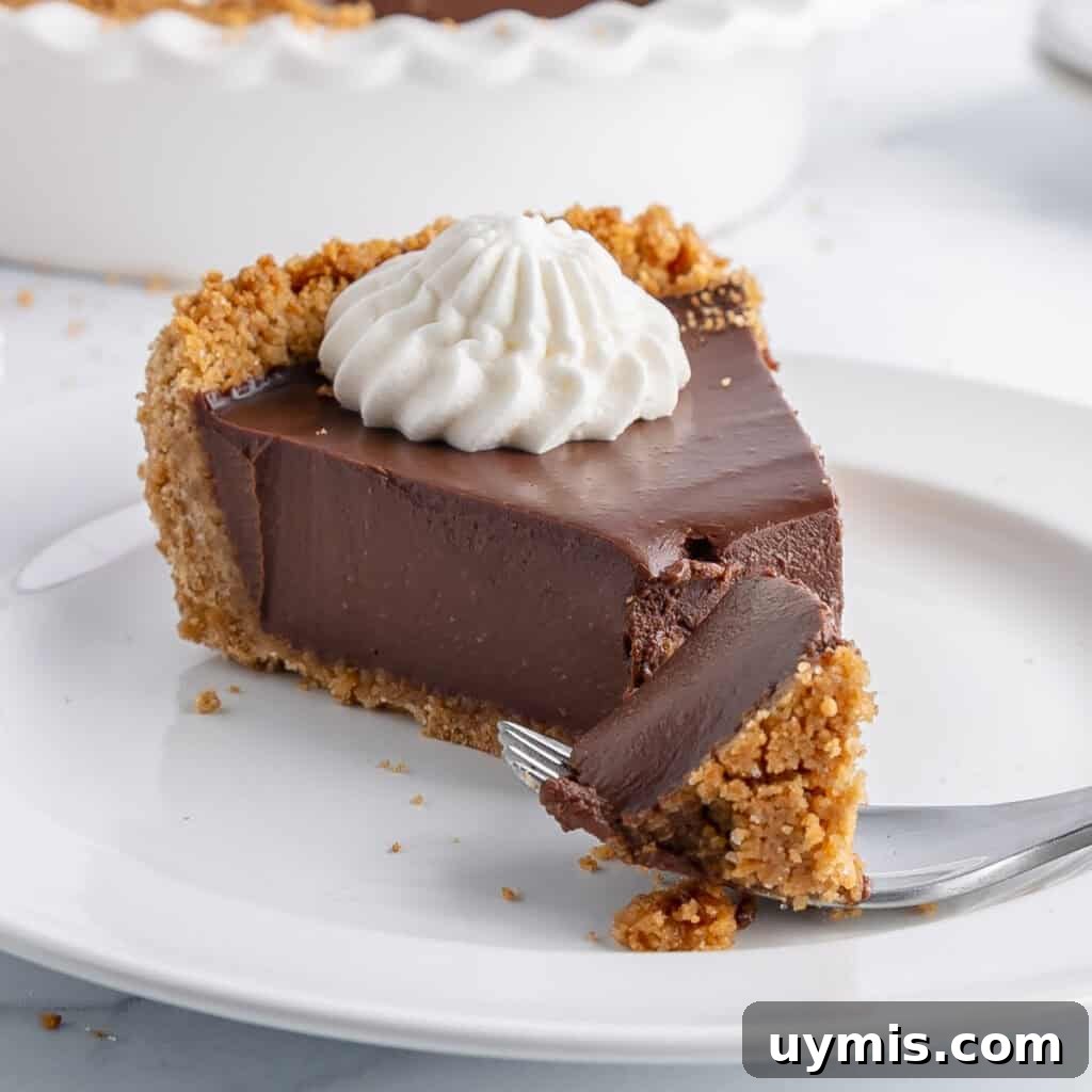 Lemon Icebox Pie Recipe with Creamy No Bake Filling 10 A slice of chocolate pie with a graham cracker crust and a dollop of whipped cream on top, served on a white plate. A fork is cutting into the pie.