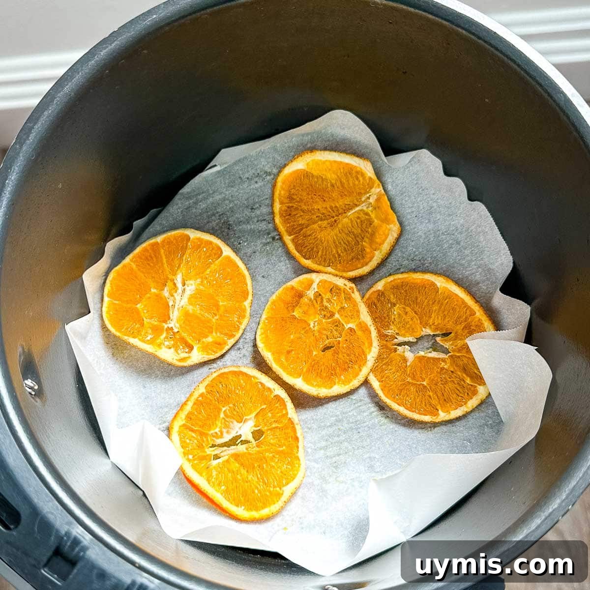 Dehydrated orange slices are shown in air fryer basket on parchment paper.