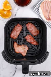 Air Fryer Canadian Bacon Breakfast Slices 14 An air fryer basket with four slices of cooked back bacon inside.