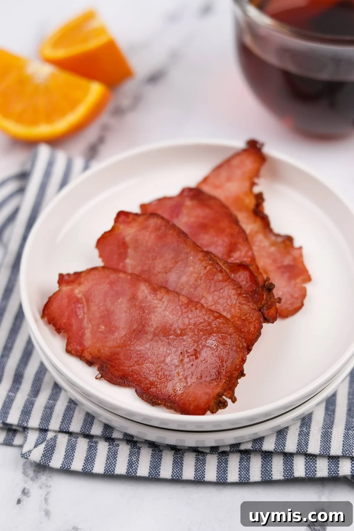 Air Fryer Canadian Bacon Breakfast Slices 6 A plate resting on a striped napkin with four slices of Canadian bacon.
