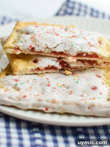 A pop tart, broken in half, resting on top of a full sized pop tart on a plate.